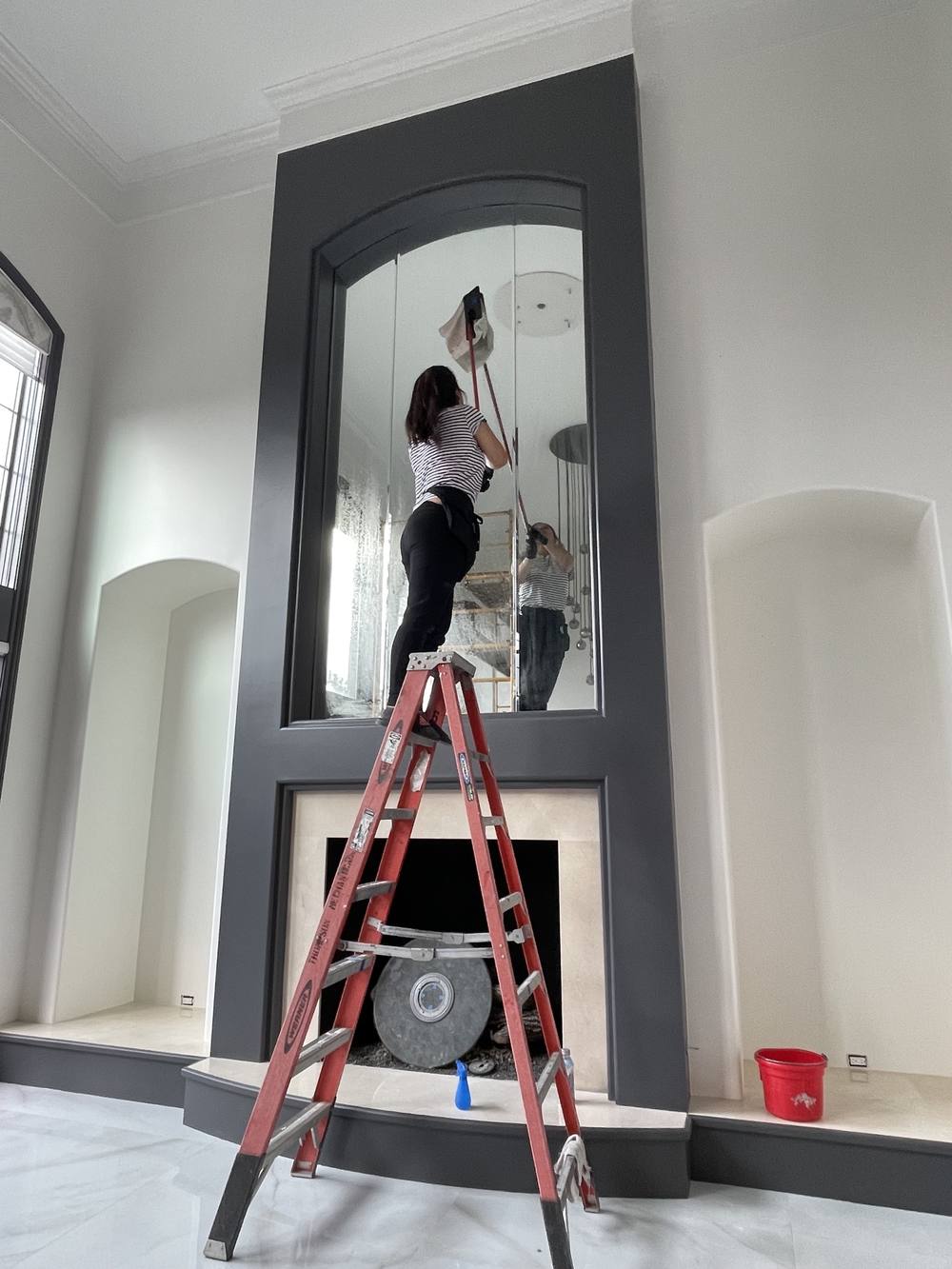 Cleaning a tall arched mirror from a ladder